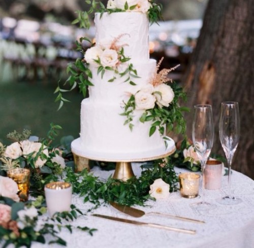 A white wedding cake adorned with greenery and flowers, creating a beautiful centerpiece for the celebration.