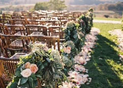 A wedding aisle with wooden chairs, greenery, and flowers.