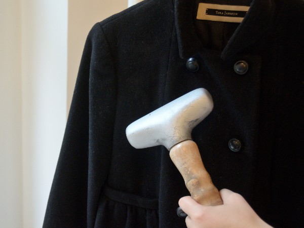 A person holding up a steamer to a black wool button-down coat.